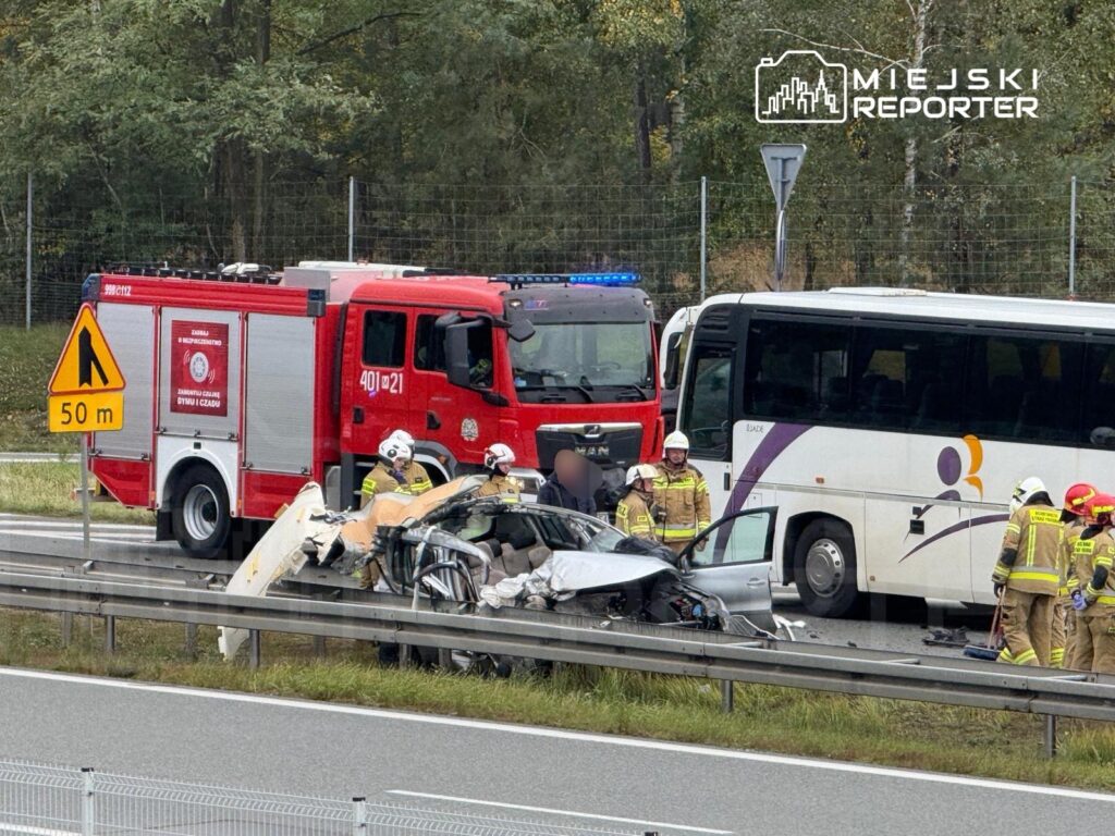 Ratownicy w kombinezonach zabezpieczają miejsce wypadku drogowego na autostradzie, obok uszkodzonego pojazdu.