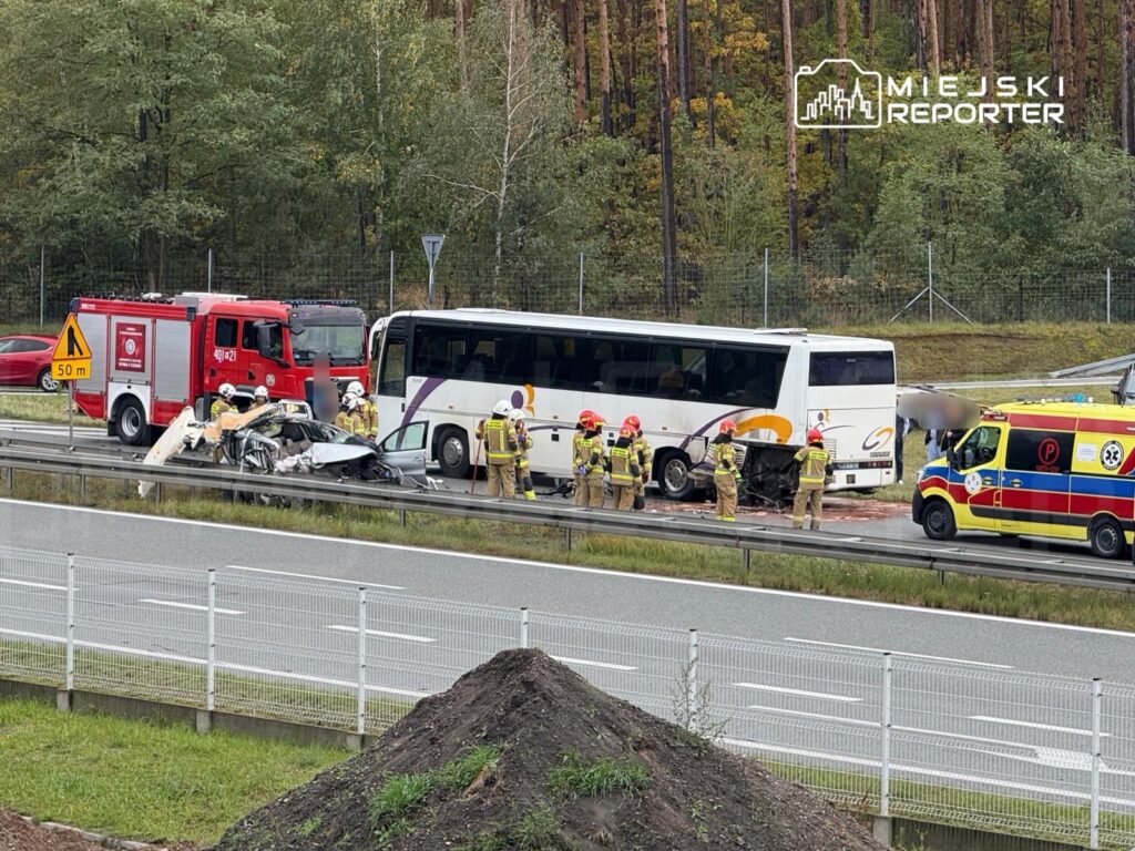 Wielu strażaków i ratowników medycznych pracuje przy wypadku drogowym, gdzie osobowy samochód zderzył się z autobusem na autostradzie.