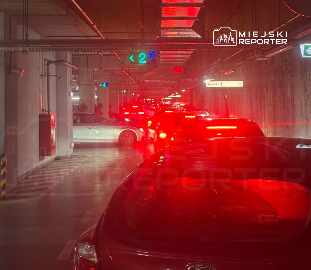 Kolejka samochodów oczekujących na wyjazd z podziemnego parkingu, oświetlona czerwonymi światłami.