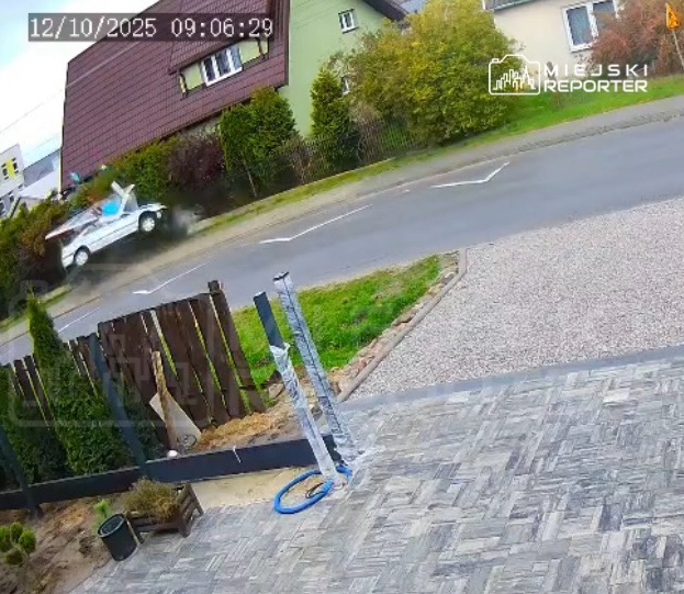 Samochód dostawczy z logo firmy jedzie po drodze, obok ogrodzenia i zieleni, w słoneczny dzień.