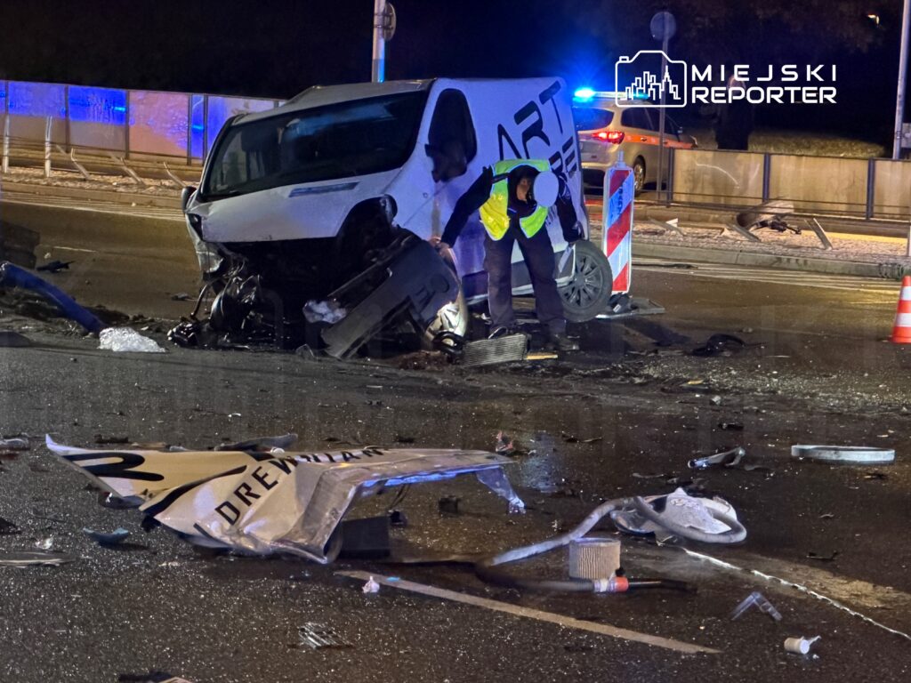Mężczyzna w kamizelce odblaskowej bada skutki wypadku samochodowego na drodze, obok uszkodzonego pojazdu.