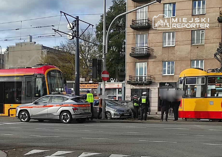 Dwa pojazdy – tramwaj i samochód osobowy – zatrzymane na skrzyżowaniu, obok interweniujący policjanci oraz zespół ratunkowy.