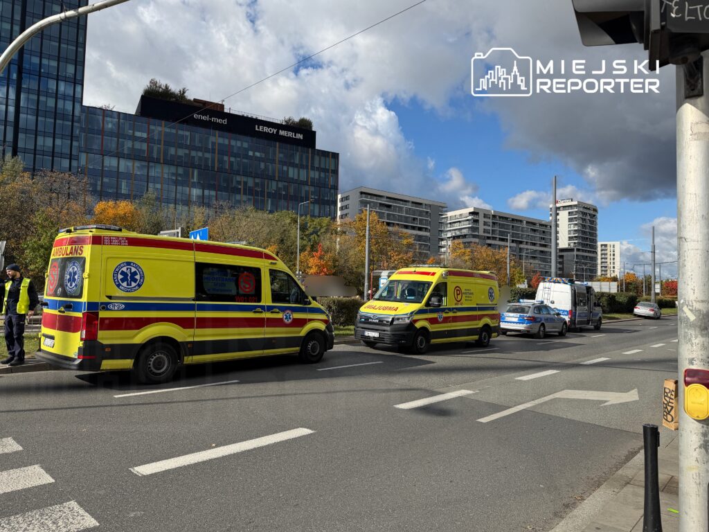 Zespół ratownictwa medycznego i policja zatrzymani na ruchliwej ulicy w pobliżu nowoczesnych budynków mieszkalnych.