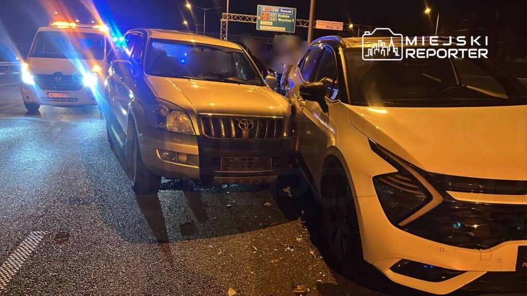 Dwa uszkodzone samochody osobowe, w tym Toyota, zderzone na drodze nocą, otoczone przez pojazdy służb ratunkowych.