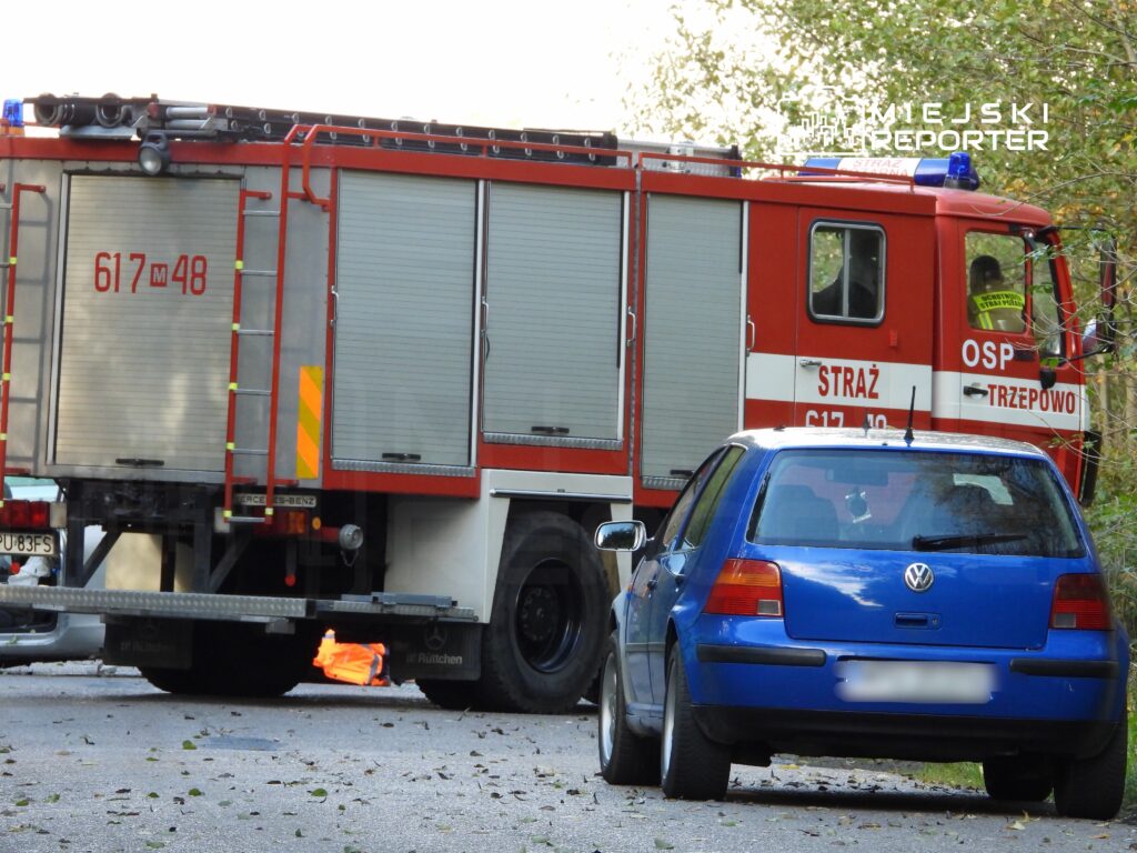 Czerwony wóz strażacki z numerem 617M48 stoi na drodze, obok niebieskiego samochodu osobowego.