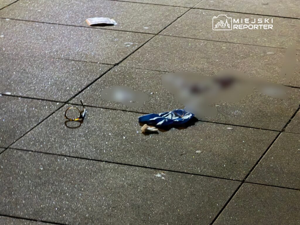 Na chodniku leżą okulary oraz niebieski materiał, wokół drobne zanieczyszczenia.