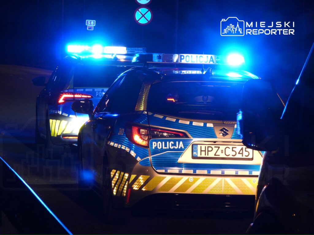 Dwa radiowozy policyjne z włączonymi sygnałami świetlnymi na ciemnej drodze.