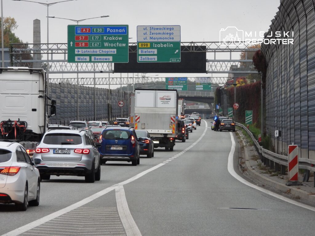 Ruch samochodowy na drodze szybkiego ruchu z oznaczeniami kierunków do Poznania, Krakowa i Wrocławia.