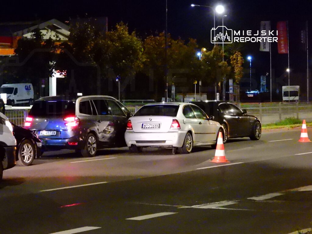 Trzy samochody zaparkowane w nocy na drodze, z pomarańczowymi pachołkami ustawionymi wokół.