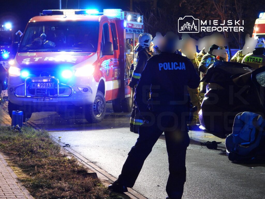 Ratownicy medyczni i strażacy pracują przy wypadku drogowym, a policjant zabezpiecza miejsce zdarzenia.