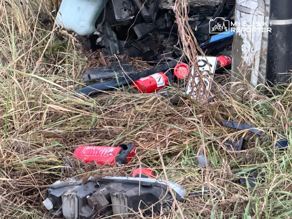 Zniszczony pojazd leży w wysokiej trawie, obok widać porzucone gaśnice i fragmenty sprzętu.