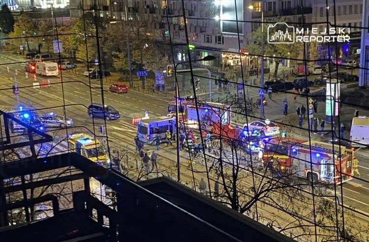 Na skrzyżowaniu ulicy z widocznymi radiowozami i pojazdami straży pożarnej z włączonymi sygnałami świetlnymi.
