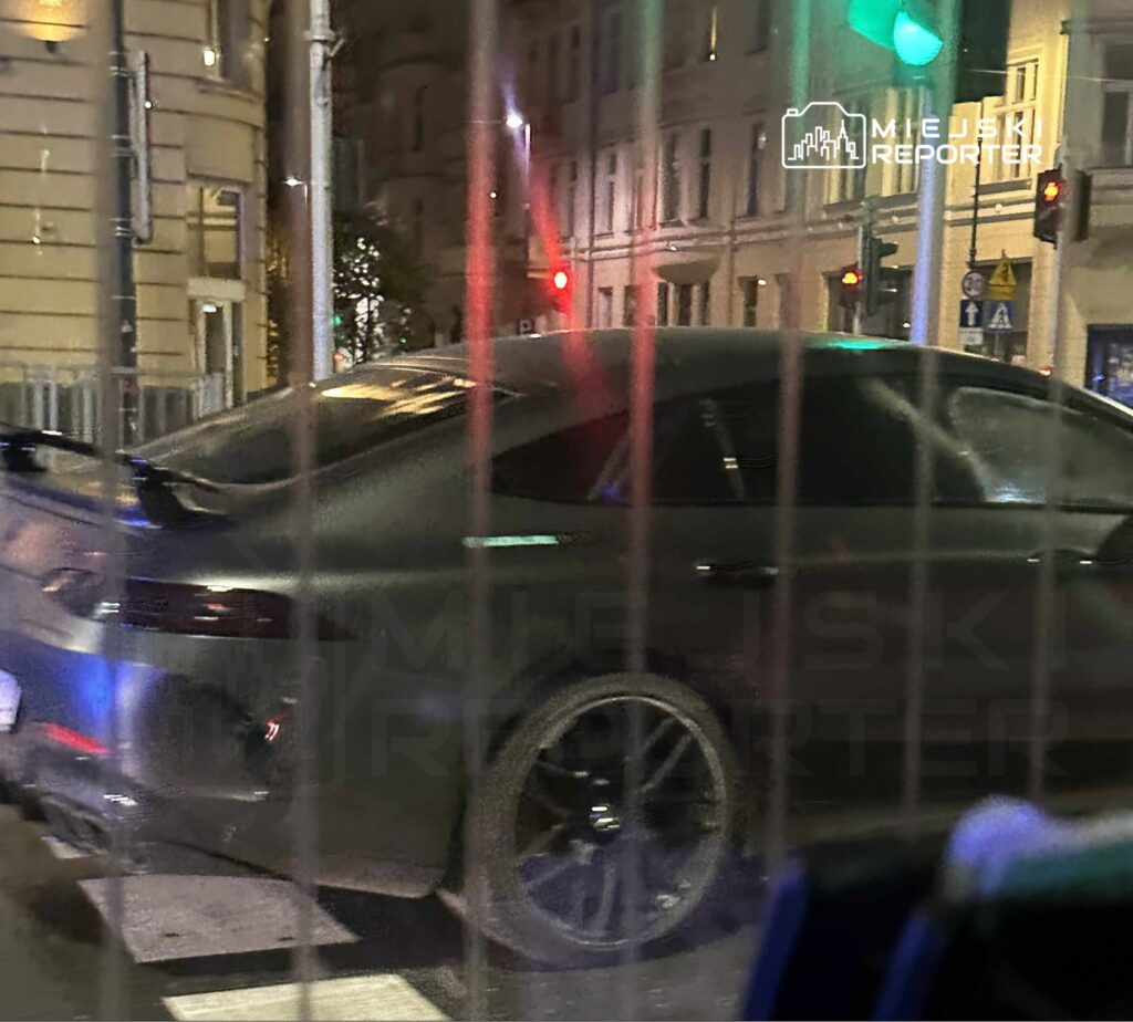 Czarny sportowy samochód zatrzymany na ulicy w nocy, obok świateł drogowych w miejskim otoczeniu.