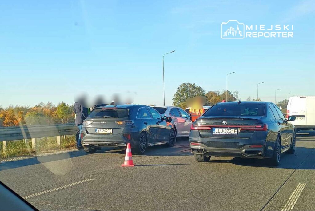 Zespół ratunkowy rozmawia z kierowcami przy zablokowanej jezdni, obok stojących samochodów osobowych.
