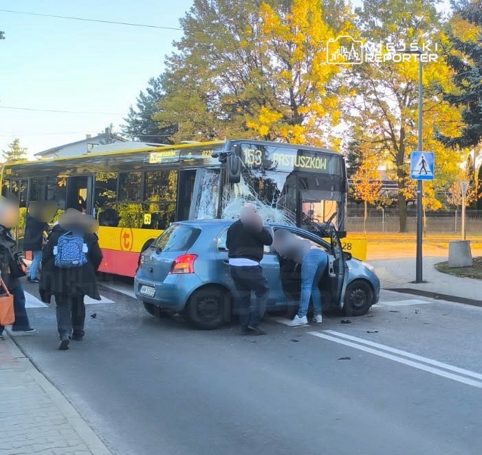 Wydarzenie drogowe: autobus z uszkodzoną szybą stoi obok niewielkiego samochodu, przy którym gromadzą się przechodnie.