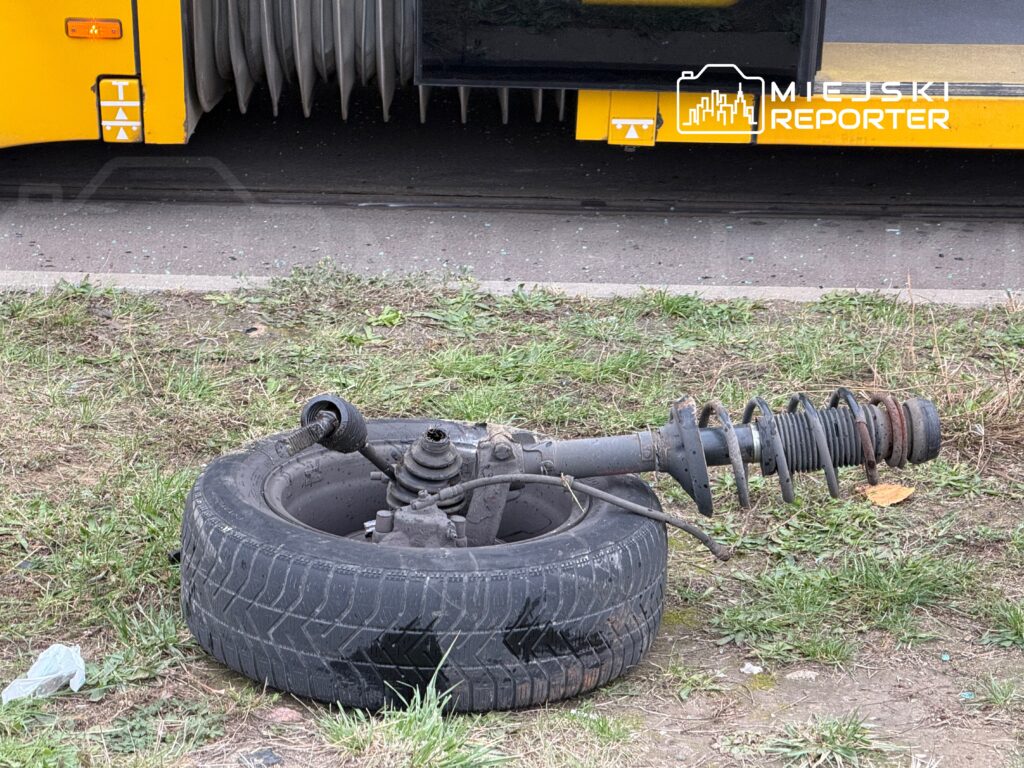 Zdemontowane zawieszenie z oponą leży na trawie obok przystanku autobusowego.