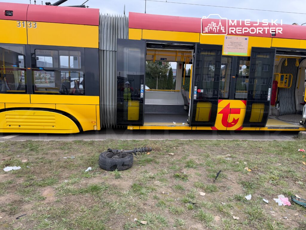 Tramwaj w żółto-czerwonych barwach zatrzymany na przystanku, z otwartymi drzwiami, obok leży uszkodzone koło.