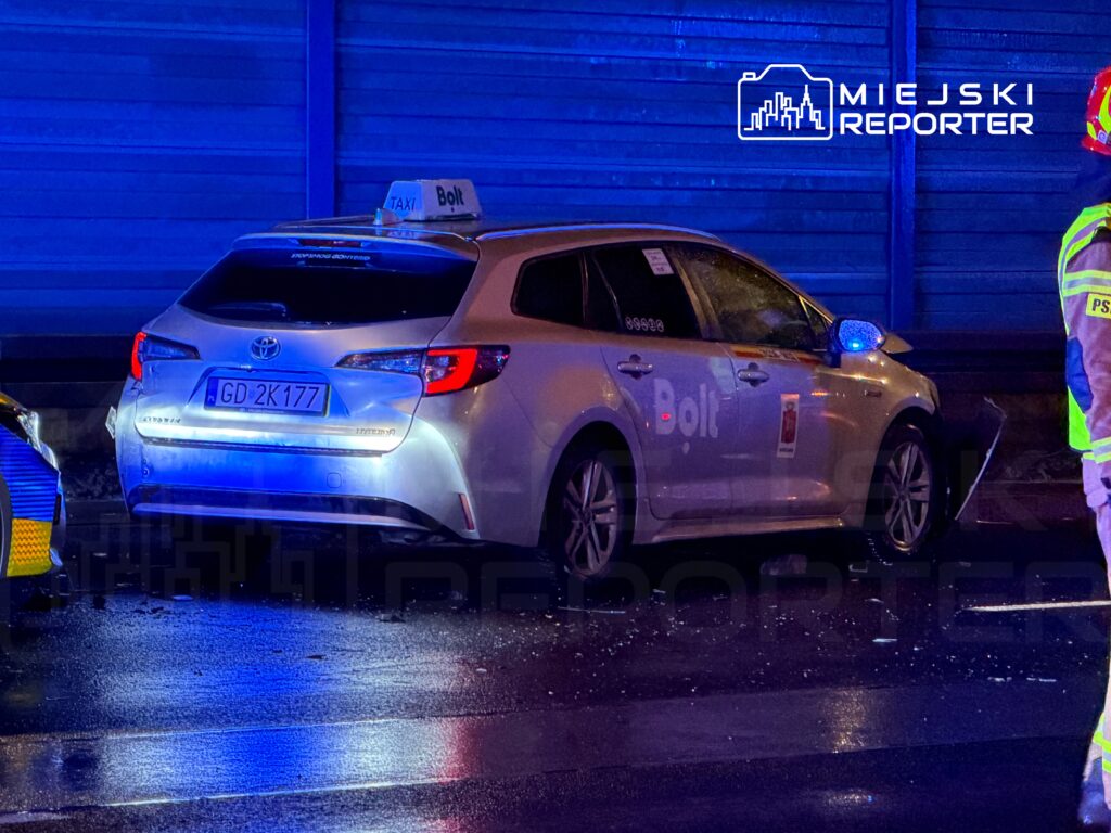Taksi marki Toyota z logo Bolt stoi na poboczu, obok niego widać funkcjonariusza w odblaskowej kamizelce.