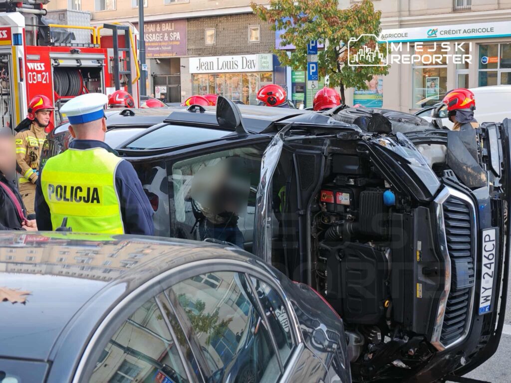 Grupa strażaków oraz policjantów przywraca porządek po wypadku drogowym, w którym przewrócił się samochód osobowy.
