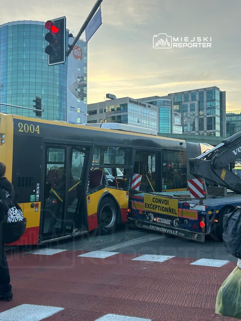Autobus miejski z numerem 2004 stoi na czerwonym świetle, obok niego znajduje się ciężarówka z napisem "CONVOI EXCEPTIONNEL".