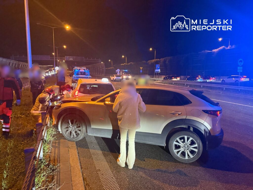 Ratownicy medyczni sprawdzają stan kierowcy przy uszkodzonym samochodzie na autostradzie w nocy.