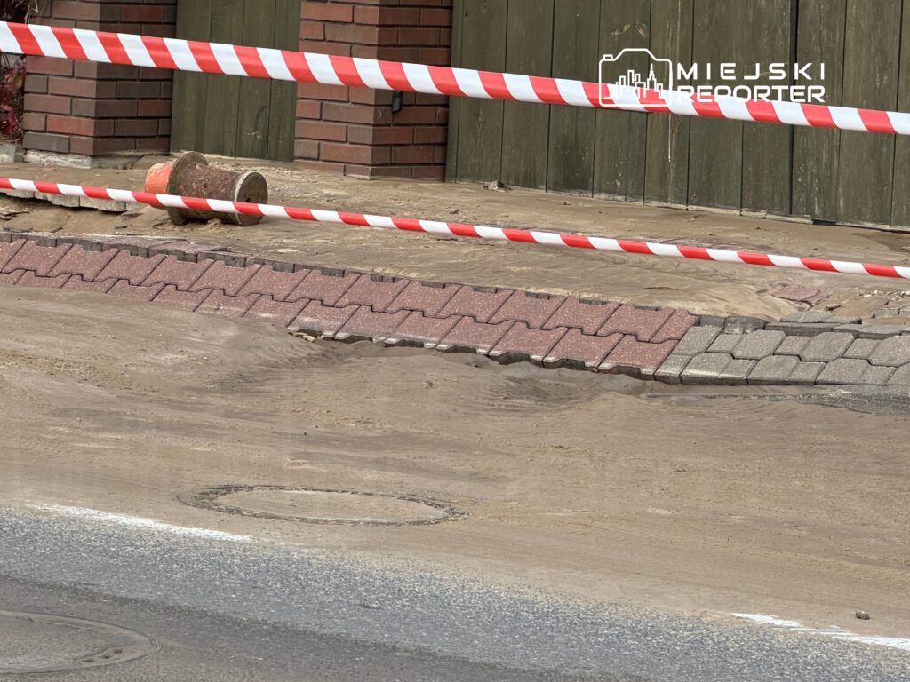 Czerwona i biała taśma ostrzegawcza otacza obszar z uszkodzoną nawierzchnią, na którym leży metalowy pojemnik.