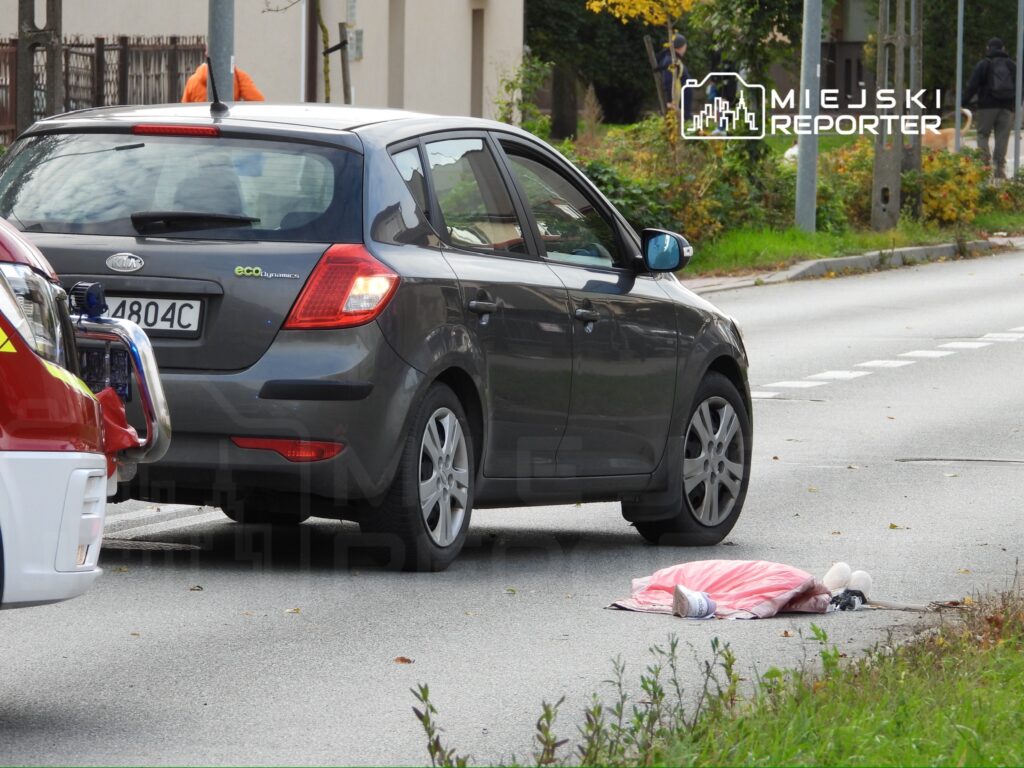 Samochód osobowy zatrzymany na drodze obok leżącego na jezdni przedmiotu przykrytego kocem.
