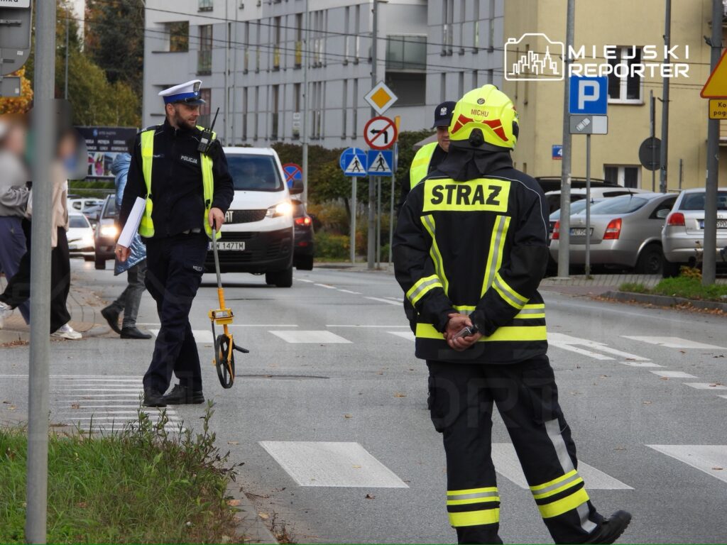 Policjant mierzy odległość na jezdni, podczas gdy strażak obserwuje sytuację w miejskiej okolicy.