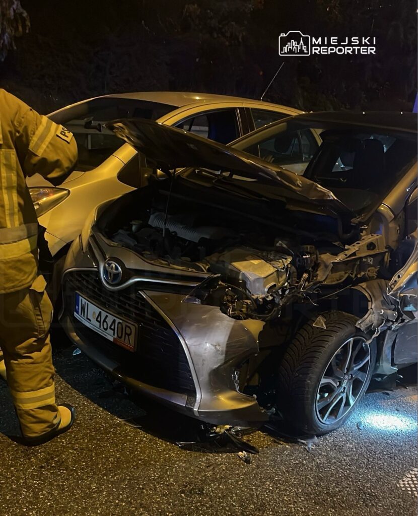 Strażak przy otwartym silniku uszkodzonego samochodu osobowego marki Toyota na drodze nocą.
