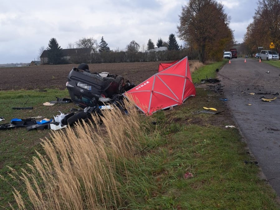 W przewróconym samochodzie leżą porozrzucane przedmioty, obok czerwony namiot i fragmenty pojazdu na poboczu drogi.