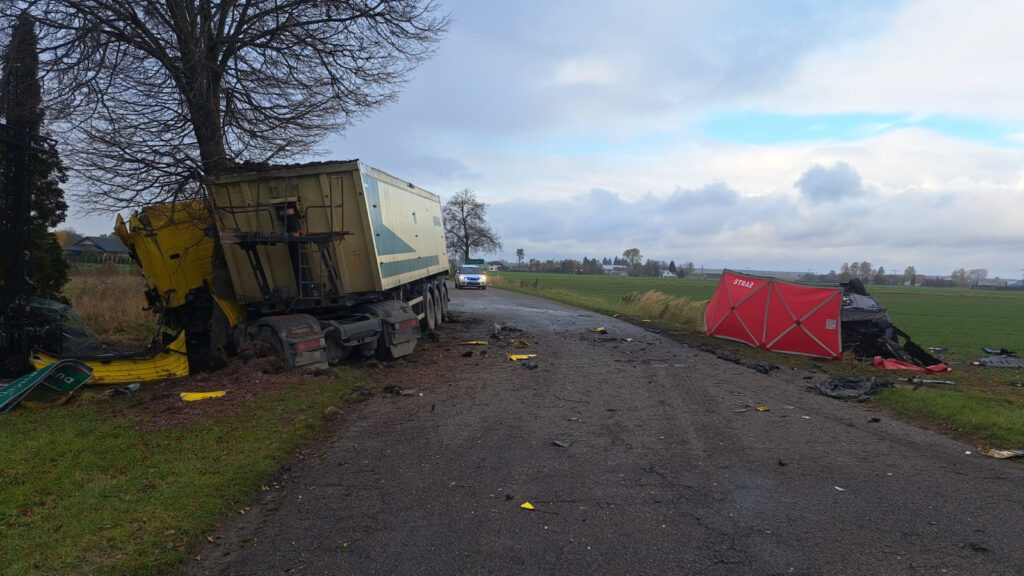 Zniszczony tir z żółtą kabiną stoi przy drodze, obok leży czerwona osłona strażacka oraz resztki wraku.