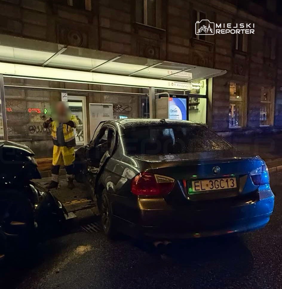 Mężczyzna w odzieży roboczej bada uszkodzone auto na ulicy przy przystanku autobusowym w nocy.