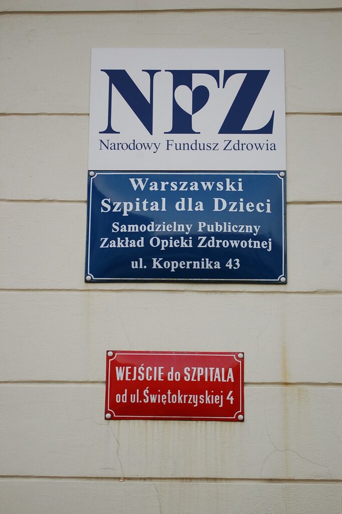 Tablice informacyjne na ścianie budynku szpitala, wskazujące na Warszawski Szpital dla Dzieci oraz wejście od ul. Świętokrzyskiej.