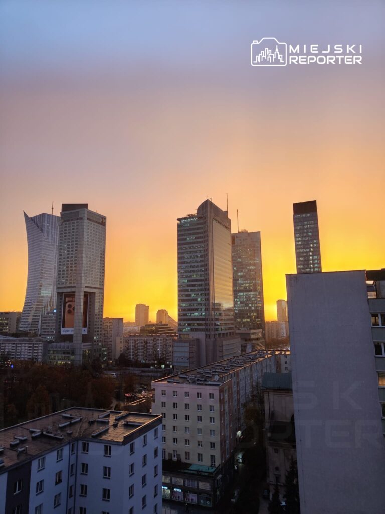 Nowoczesne wieżowce odbijające pomarańczowe światło zachodzącego słońca w miejskiej scenerii.