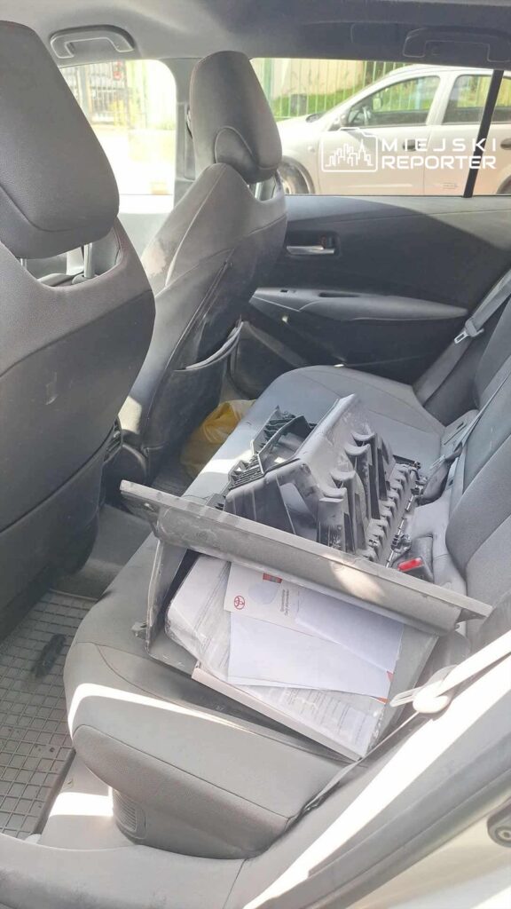 Wnętrze samochodu z widoczną odłożoną częścią plastikową oraz papierami na tylnym siedzeniu.