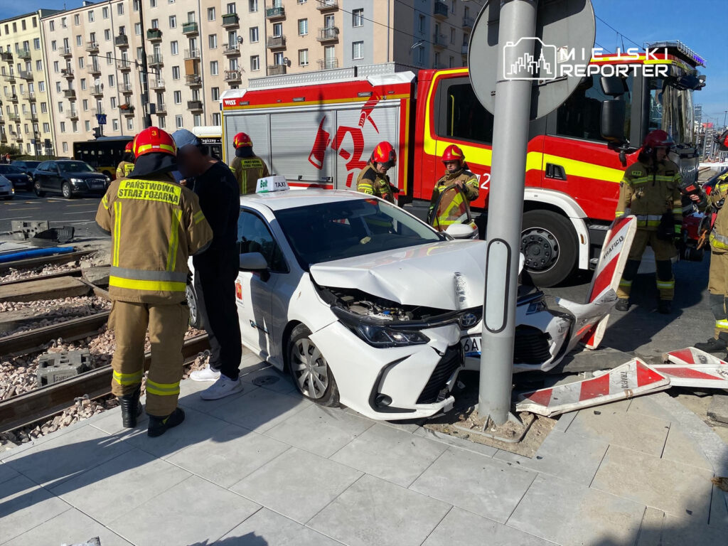 Strażacy udzielają pomocy kierowcy taksówki, która uderzyła w słup, obok torów tramwajowych.
