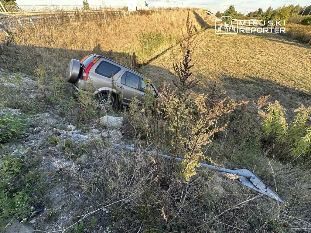 Samochód terenowy utknął w zaroślach przy drodze, obok widoczna uszkodzona bariera ochronna.