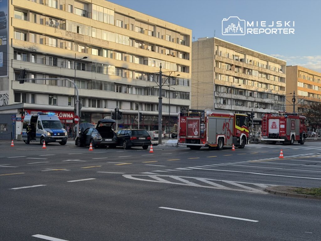 Na skrzyżowaniu stoją trzy pojazdy służb ratunkowych, w tym karetka i dwa wozy strażackie, otoczone pachołkami drogowymi.
