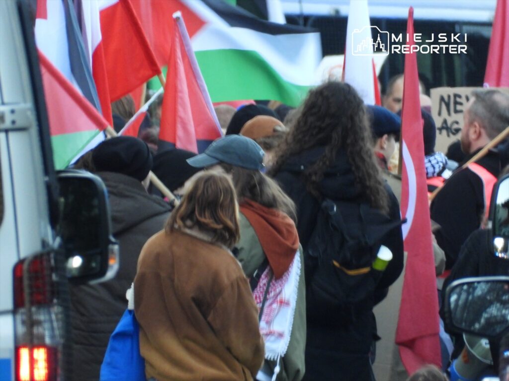 Grupa demonstrantów trzymająca flagi różnych krajów, protestująca na ulicy w miejskim otoczeniu.