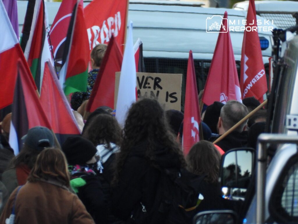 Tłum ludzi z flagami w rękach, wśród nich dziecko, trzymające transparent z napisem „EVERY HUMAN IS...”.