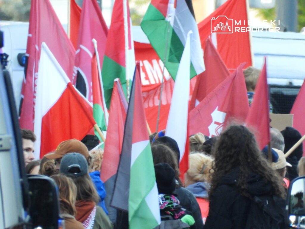 Grupa ludzi trzymająca różnokolorowe flagi, w tym polską, podczas demonstracji na ulicy.