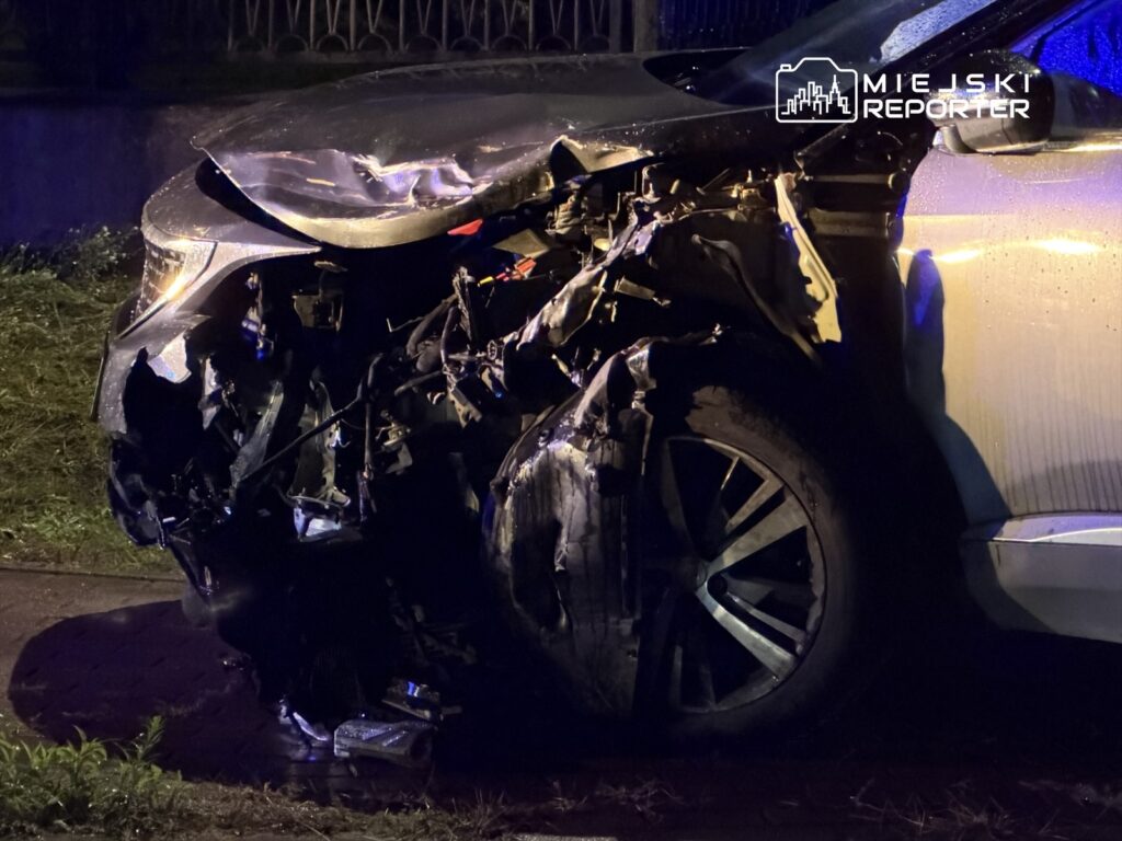 Uszkodzony samochód osobowy z poważnymi zniszczeniami przodu, zaparkowany w ciemnej okolicy.