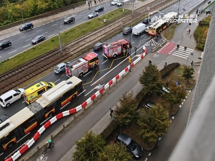 Ruch uliczny zablokowany przez kilka wozów strażackich i ambulans, na drodze z barierkami wzdłuż chodnika.