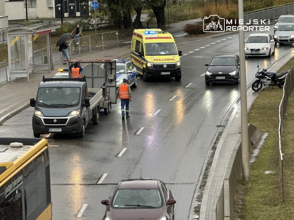 Na ulicy zatrzymane pojazdy, w tym karetka i samochód dostawczy, obok pracownik w pomarańczowej kamizelce kieruje ruchem.