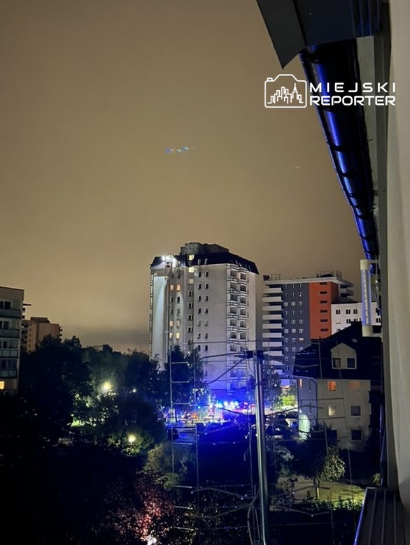 Nocne niebo z widocznymi kolorowymi światłami nad nowoczesnymi budynkami w miejskim otoczeniu.