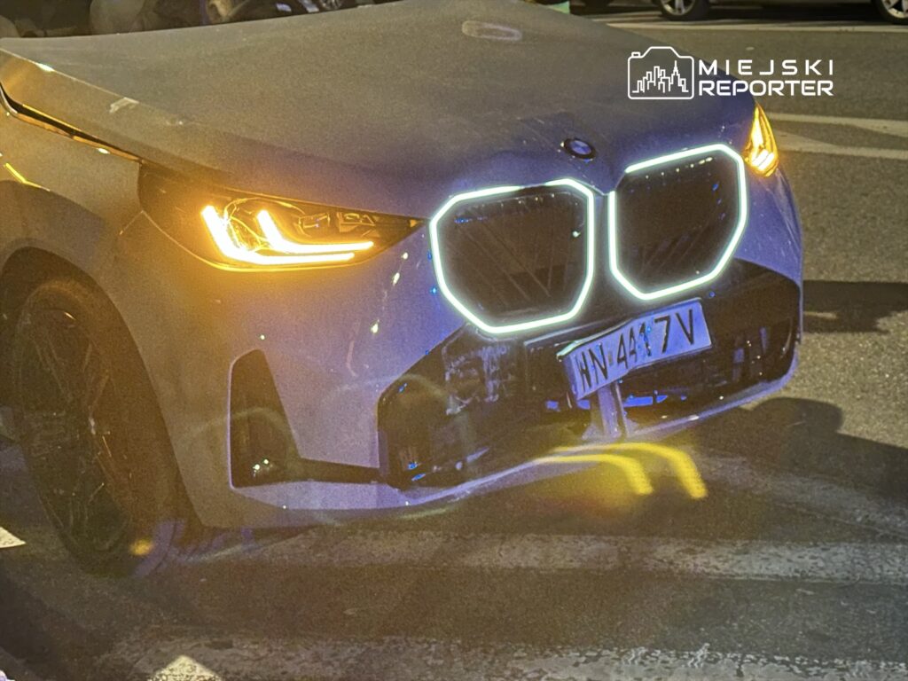 Nowoczesny samochód marki BMW z podświetlonym grillem stoi na ulicy nocą, w tle widać miejskie światła.