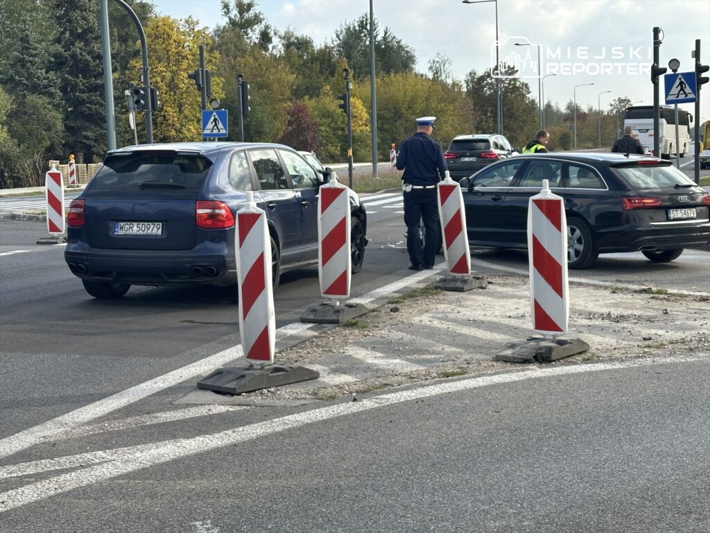 Policjant rozmawia z kierowcą przy zatrzymanym samochodzie na skrzyżowaniu z sygnalizacją świetlną.