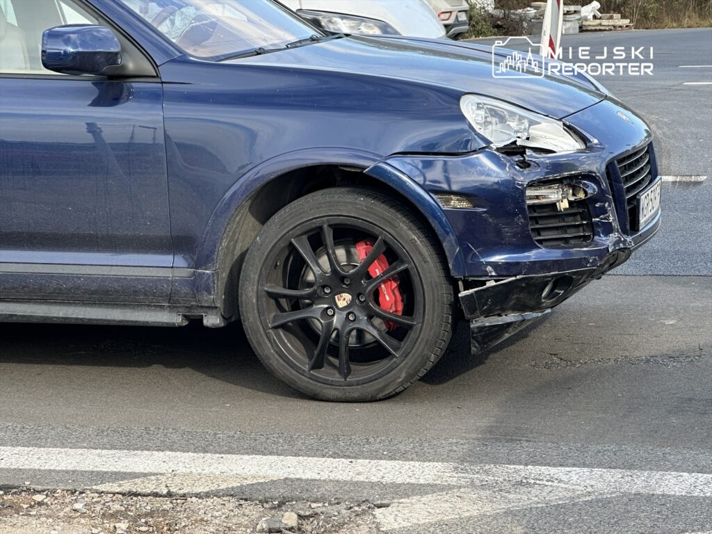 Uszkodzony niebieski samochód osobowy z czarnymi felgami stoi na drodze, z widocznymi uszkodzeniami przedniego zderzaka.