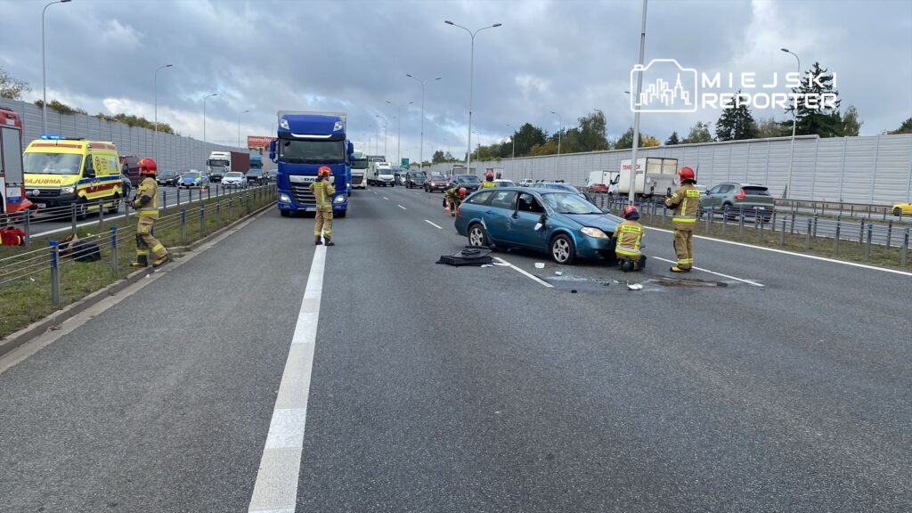 Strażacy udzielają pomocy przy wypadku drogowym na autostradzie, obok uszkodzonego samochodu osobowego.