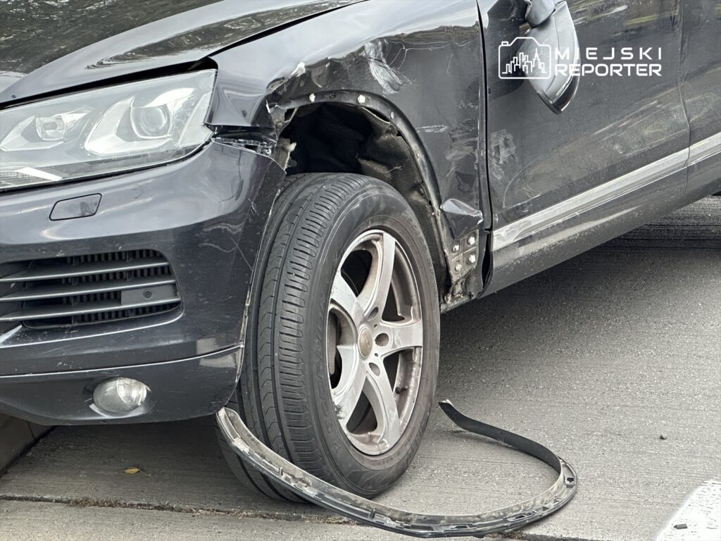 Uszkodzony samochód osobowy z rozdartą oponą oraz wgniecioną karoserią stoi na drodze.